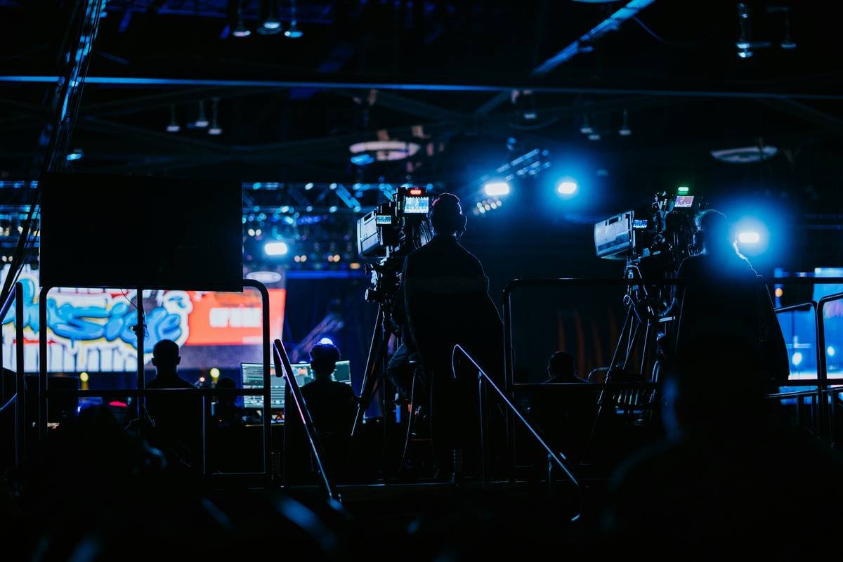 Professional gamers sitting on stage with glowing keyboards and large monitors.
